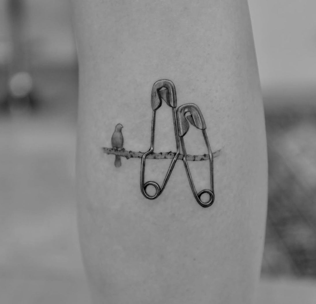 Two safety pins and a small bird on a thin branch.